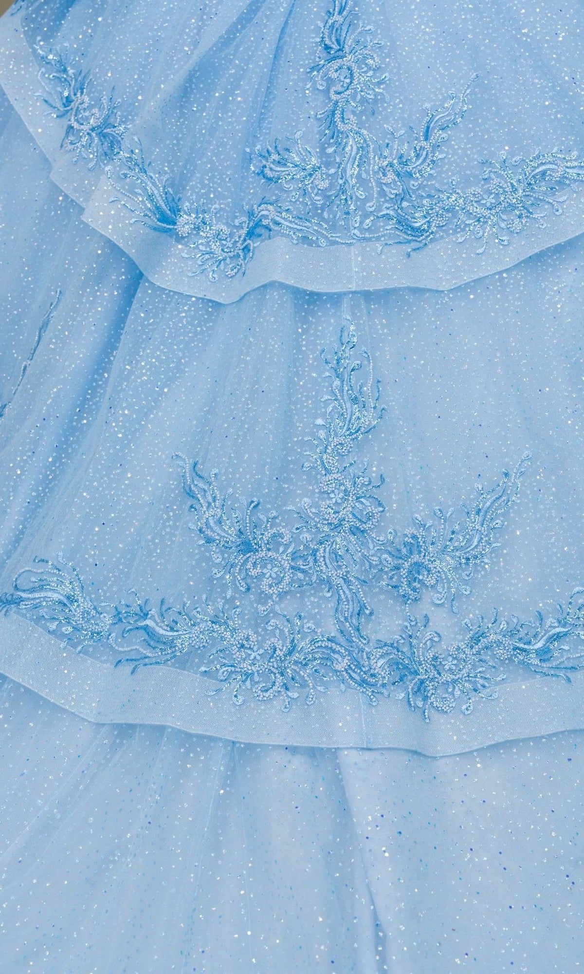 Close-up of a light blue, sparkly fabric with embroidered floral patterns and layered ruffles, reminiscent of the dazzling Quinceanera Dress 8520JQ by Cinderella Couture.